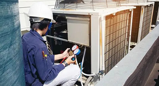 A technician using gauges to service an outdoor AC unit on a rooftop