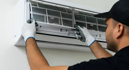 A technician inspecting filters in a wall-mounted ductless mini-split AC unit