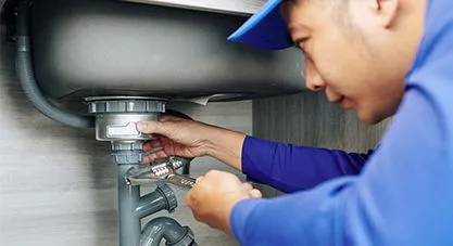 A plumber inspecting a sink drain, tightening a pipe with a wrench