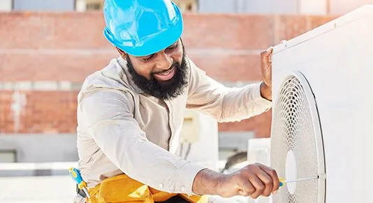 A smiling HVAC technician working on an outdoor air conditioning unit