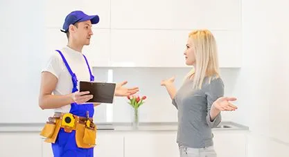 A plumber discussing an issue with a homeowner, who appears concerned, in a modern kitchen setting