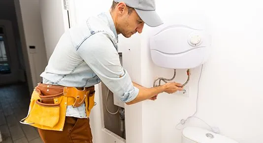 A technician servicing a compact, wall-mounted water heater, carefully connecting its pipes