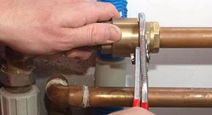 A plumber's hands using a wrench on a brass fitting connecting copper pipes