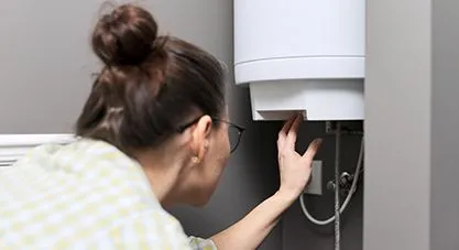 A woman carefully inspecting the bottom of a white water heater,