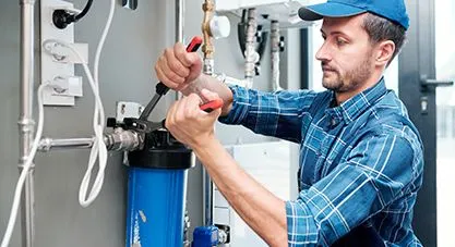 A First Service plumber installing a water filter, using pliers on the blue filtration unit