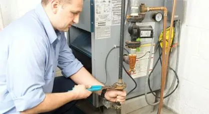 A First Service technician using a wrench to perform maintenance on a heating unit