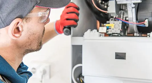 A technician wearing safety glasses performing maintenance on the intricate internal components of a commercial furnace