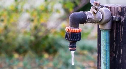 An outdoor faucet with a connected hose dripping a small icicle