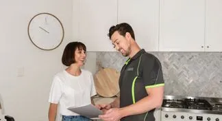 A First Service technician discussing documents with a smiling customer in her modern kitchen