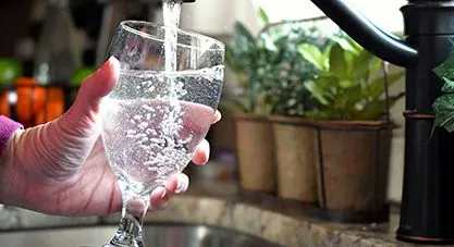 A hand fills a clear glass with bubbly tap water from a kitchen faucet