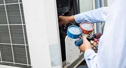 An HVAC technician connecting red and blue gauges to an outdoor unit