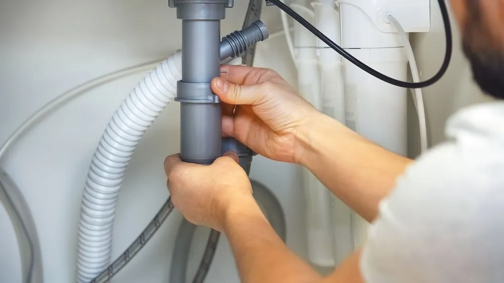 A plumber connecting grey PVC plumbing pipes under a sink