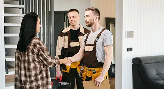 A homeowner warmly greets two service technicians in their home