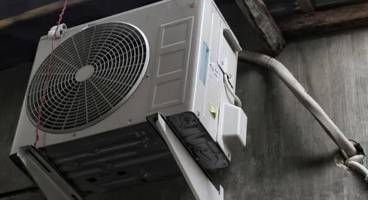An outdoor white AC condenser unit mounted on a concrete wall